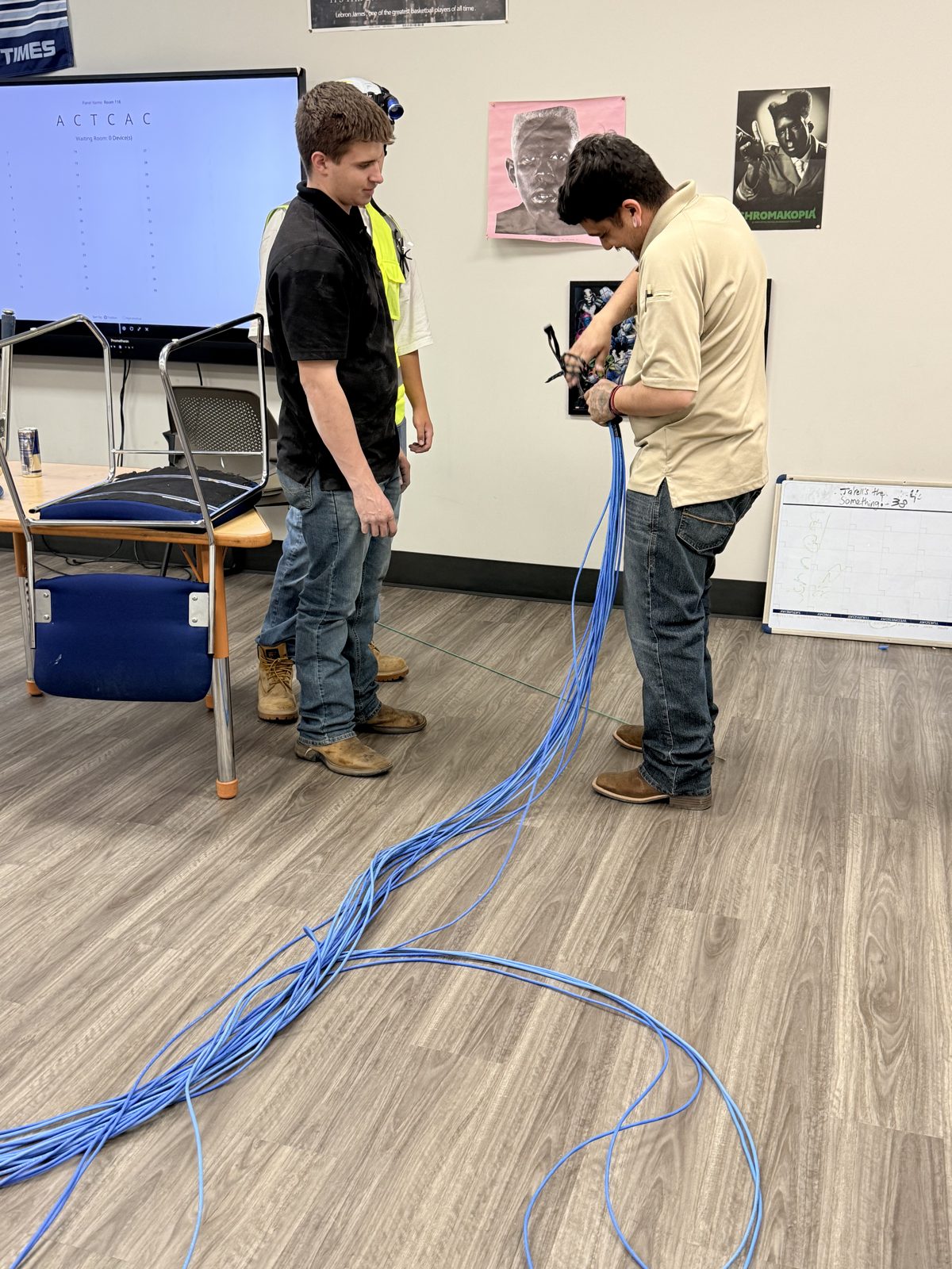 Two HPSI technicians hand-bundling blue Cat6 cable runs at a school
